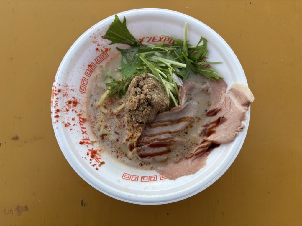 ラーメンエキスポで販売されていた、赤いスパイスがかかったラーメンと大きなチャーシューの写真。