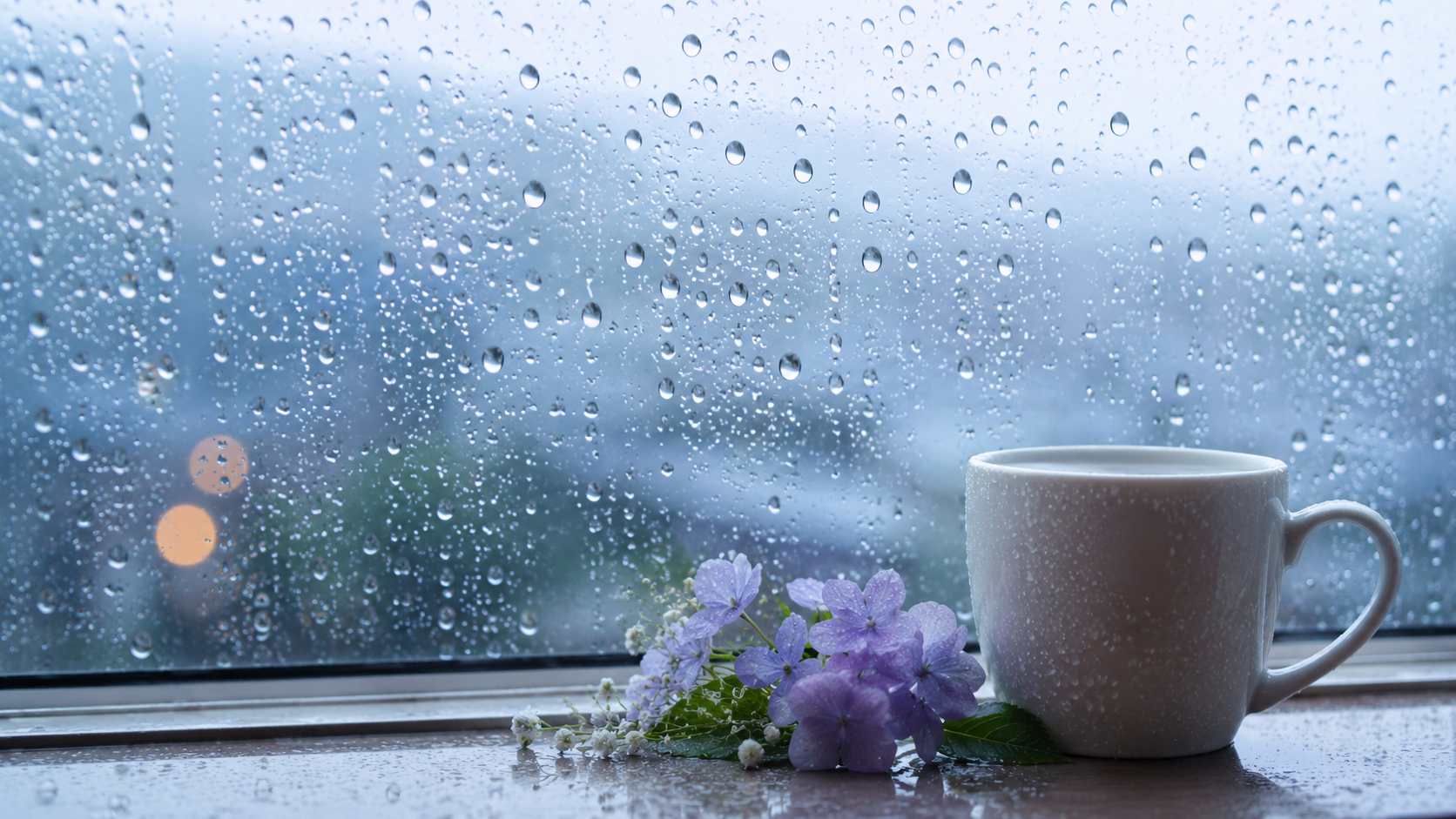 雨粒のついた窓と温かい飲み物のある雨の朝